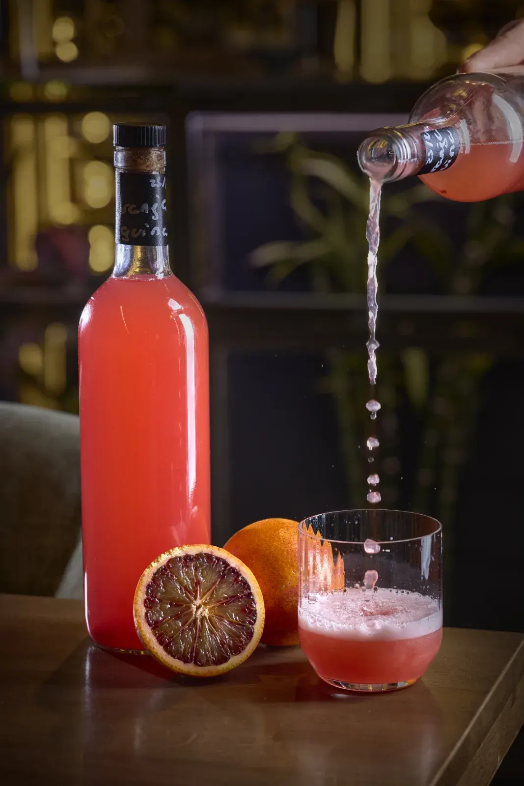 Bebida de naranja sanguina sirviéndose junto a la fruta abierta